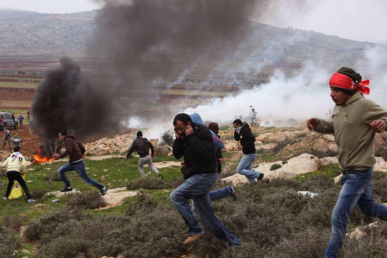 Activistas palestinos huyen de los gases lanzados por las fuerzas de seguridad israelíes durante una protesta al norte de Ramala contra los asentamientos judíos