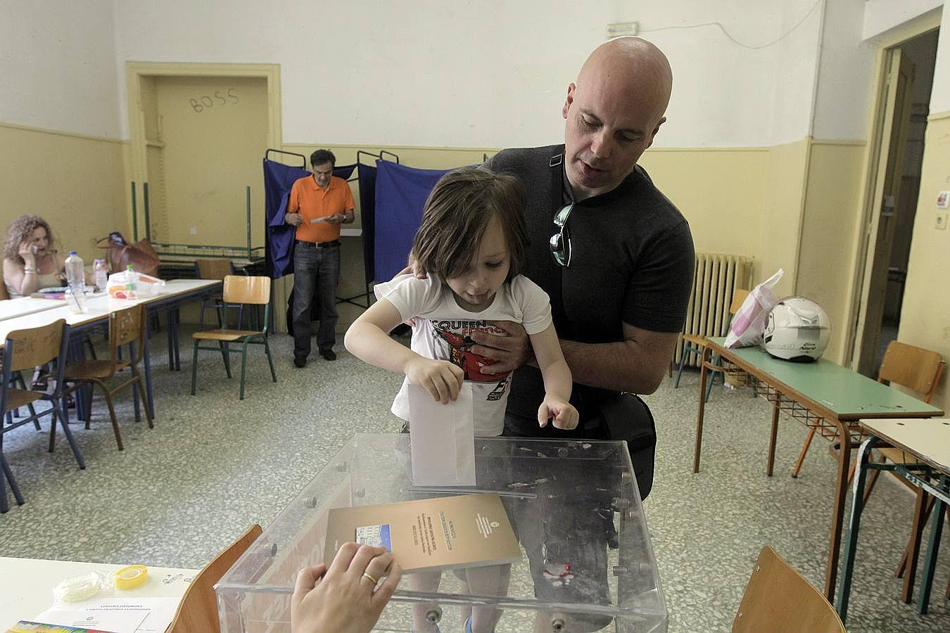 Un griego deja que su hija deposite su papeleta en la urna electoral